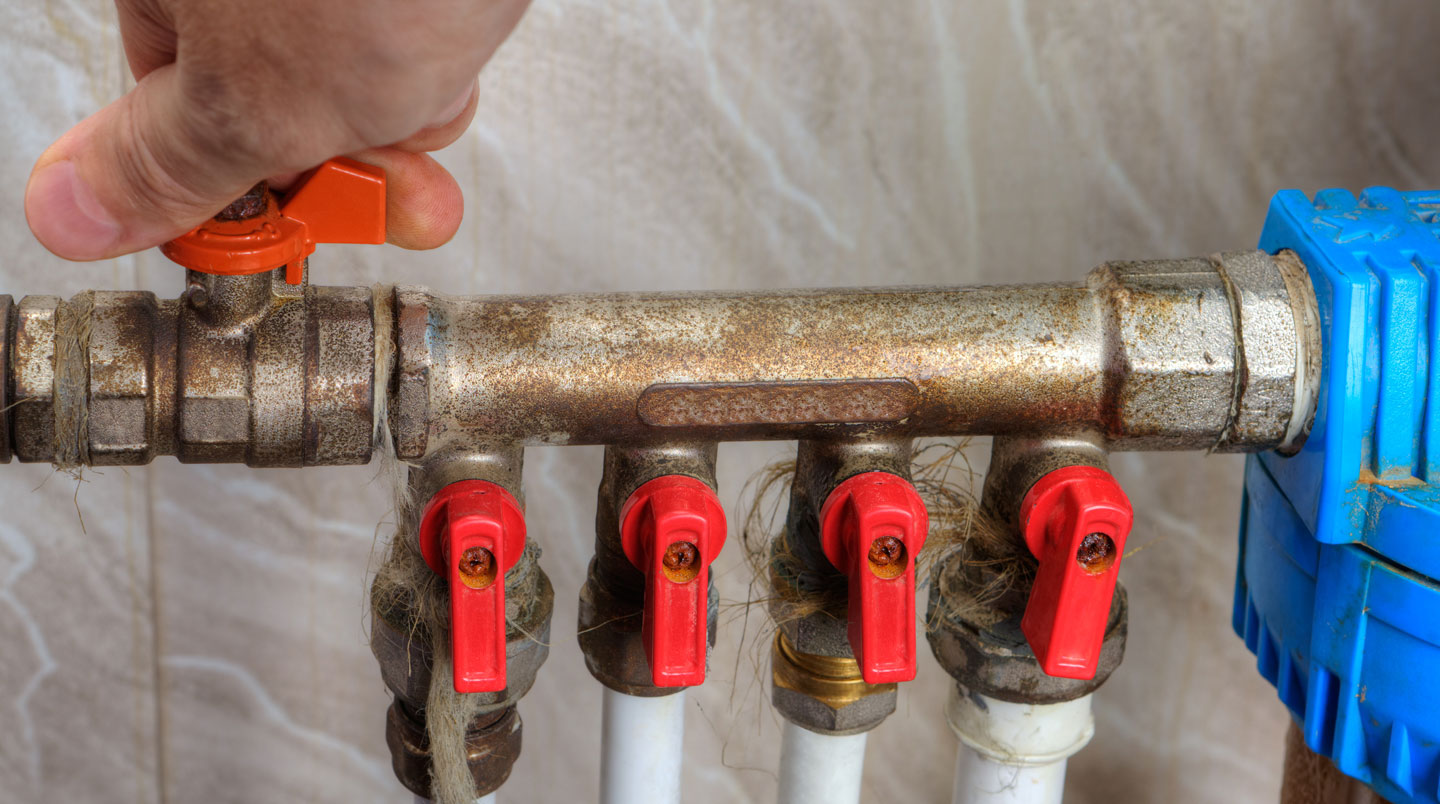 Sous-sol résidentiel montrant un robinet d'arrêt principal en laiton sur tuyau d'alimentation, avec étiquette 'Robinet principal' et chauffe-eau en arrière-plan